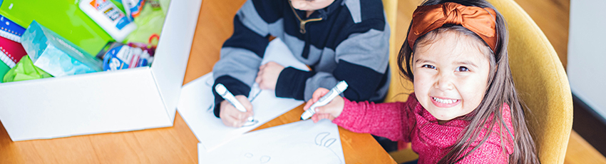 Young girl smiles at camera holding marker